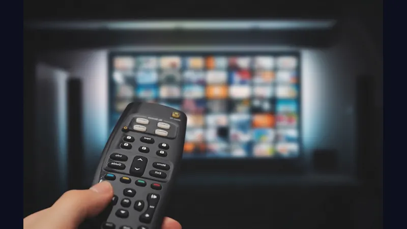 Hand holding a television remote in front of a big screen